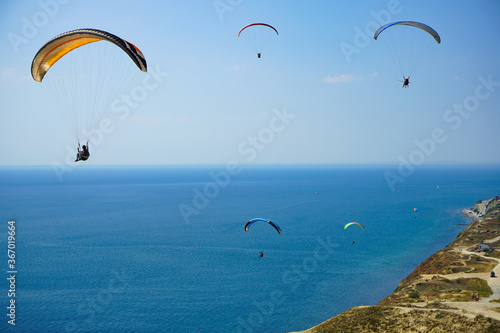 Paragliders soar on beautiful paragliders against the background of blue sky and blue sea, shot from the top of the mountains © Natalia Tarasova