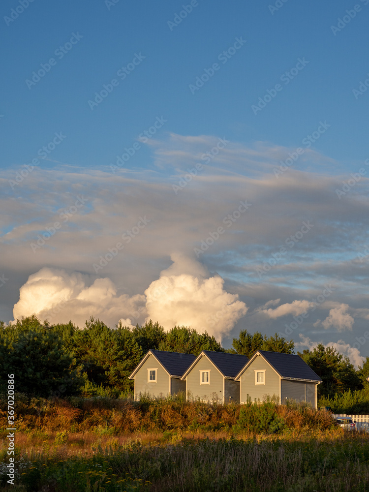 3 identical small wooden houses stand side by side in the sunset and the sky is cloudy