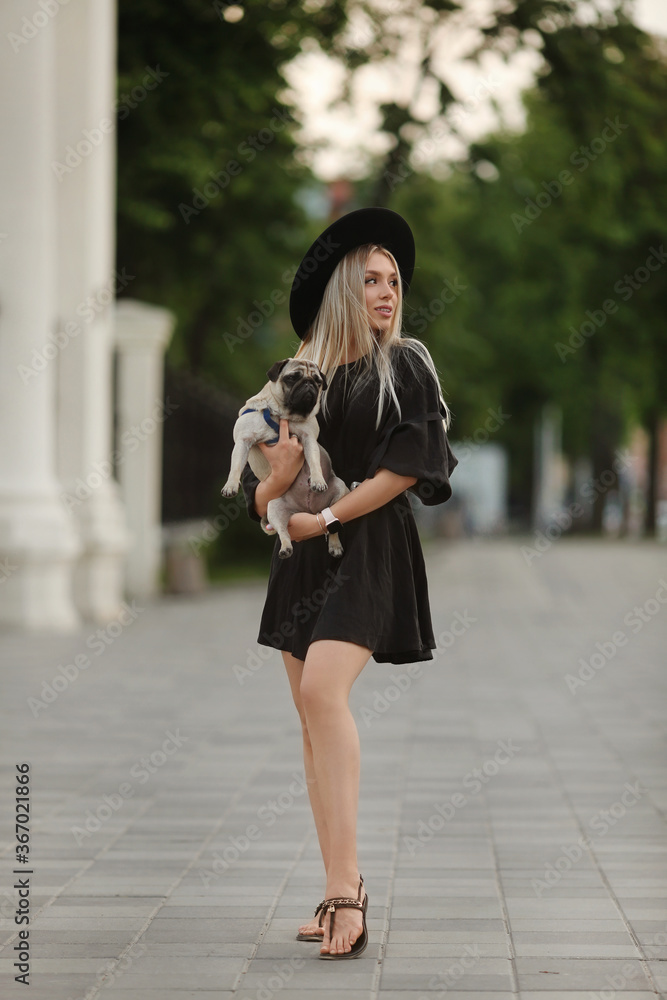 A young beautiful model girl in short summer dress joyfully walking on a city street with her small cute dog