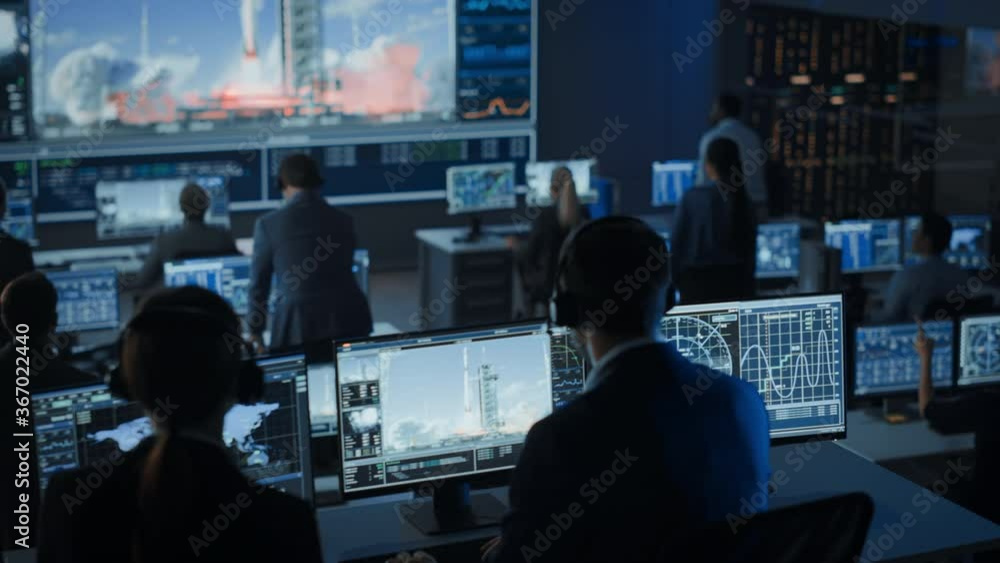Group of People in Mission Control Center Witness Successful Space Rocket Launch. Flight Control Employees Sit in Front Computer Displays and Monitor the Crewed Mission. Team Stand Up and Clap Hands. Group of People in Mission Control Center Witness Successful Space Rocket Launch. Flight Control Employees Sit in Front Computer Displays and Monitor the Crewed Mission. Team Stand Up and Clap Hands.