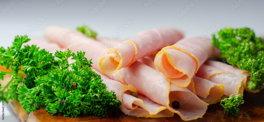 Sliced cooked ham with curly parsley on a wooden board