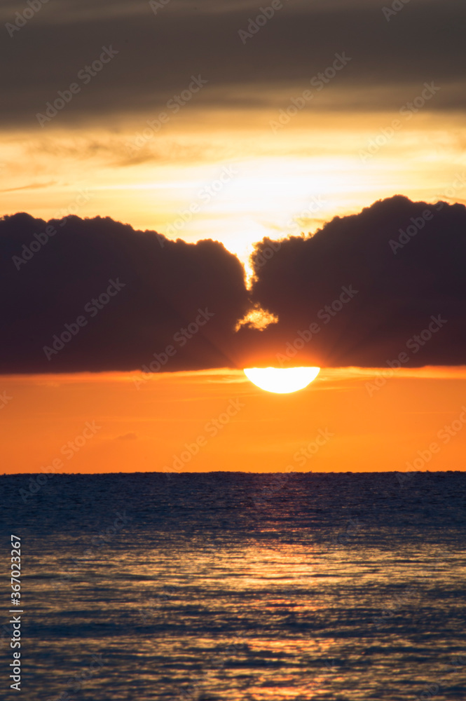 Sun rising from the sea between two clouds and the sea with soft waves bathing the shore of the beach behind the dawn clouds