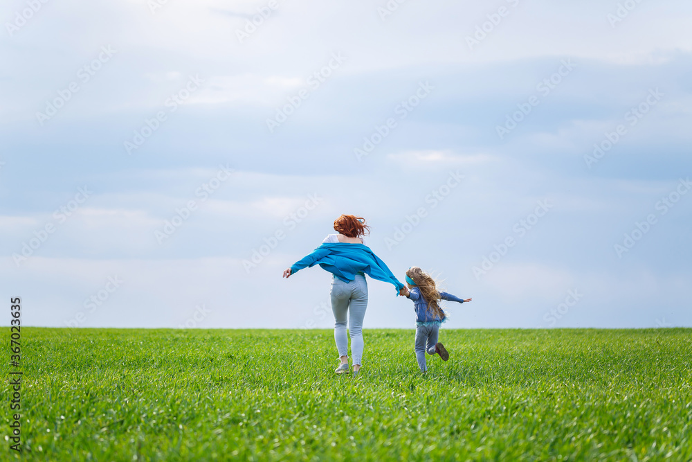 little girl child and mother woman run and jump, green grass in the field, sunny spring weather, smile and joy of the child, blue sky with clouds little girl child and mother woman run and jump, green grass in the field, sunny spring weather, smile and joy of the child, blue sky with clouds