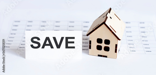 Closeup of house wooden model with blank for text SAVE on chart background.