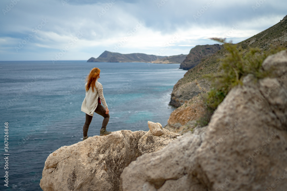 Rear view of woman looking at sea against sky while standing on rock