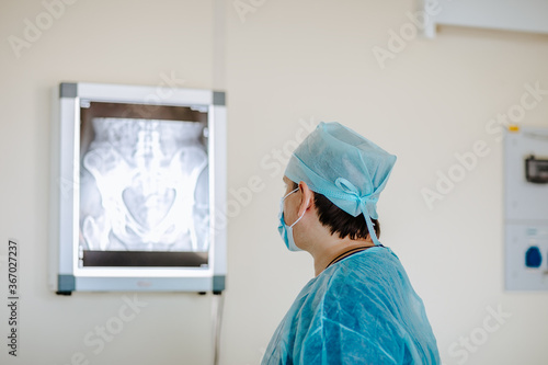 Adult white doctor posing near the x-rayed at the white operation room. Copy space.