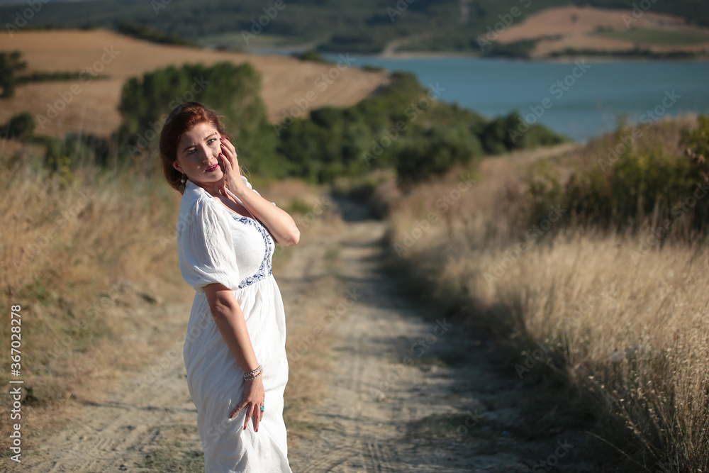 Young brunette woman in short white dress walking by a rural road Young brunette woman in short white dress walking by a rural road