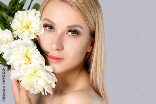Portrait of a beautiful blonde woman with long hair  beautiful fresh makeup and healthy clean skin with peonies in her hands. Makeup and cosmetology concept.