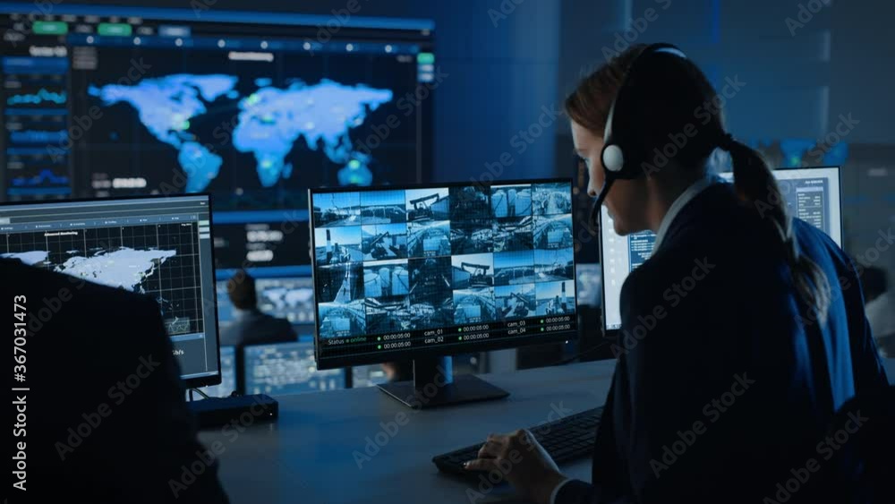 Female Officer Works on a Computer with Surveillance CCTV Video Footage in a Police Monitoring Center with Global Map Tracking on a Big Digital Screen. Employees Sit in Front of Displays with Big Data Female Officer Works on a Computer with Surveillance CCTV Video Footage in a Police Monitoring Center with Global Map Tracking on a Big Digital Screen. Employees Sit in Front of Displays with Big Data