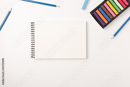 Colored wax crayons, sketchbook isolated on white background. Colorful chalk. Flat lay, top view, copy space.