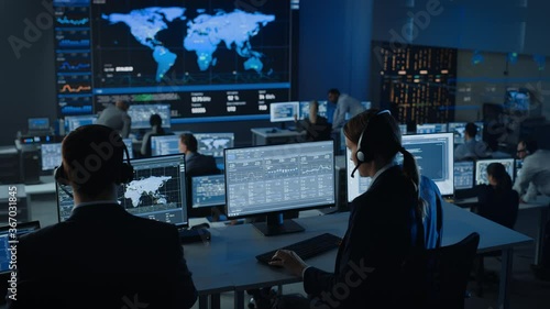 Female Specialist Works on a Computer with Live Ananlysis Feed from a Global Map on a Big Digital Screen. Employees Sit in Front of Displays with Financial Stock Market Trading Info and Big Data. photo