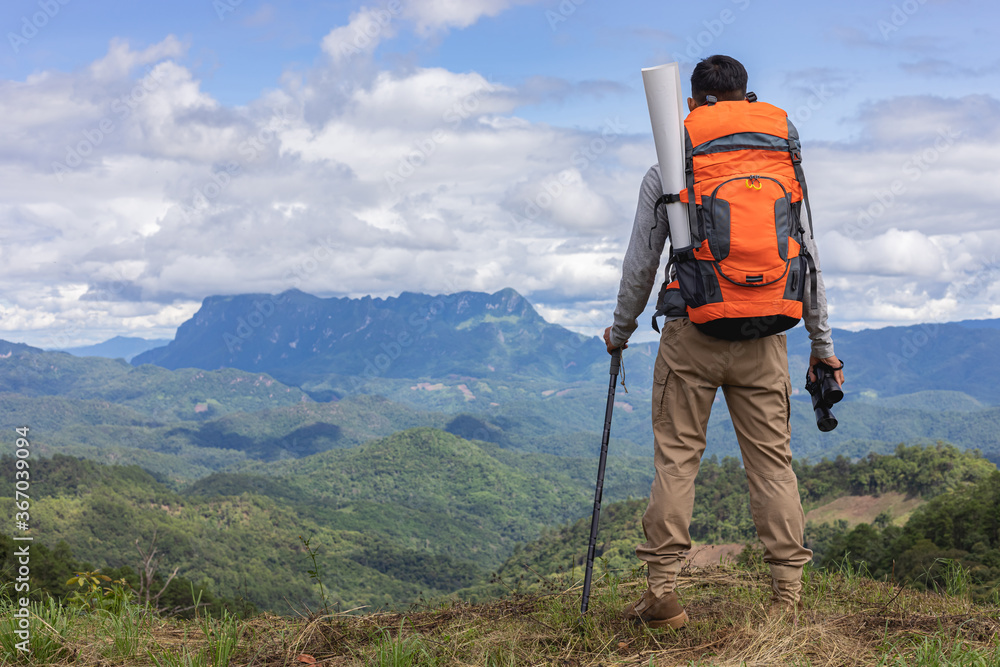 Young man with backpack and holding a binoculars looking on top of mountain layered