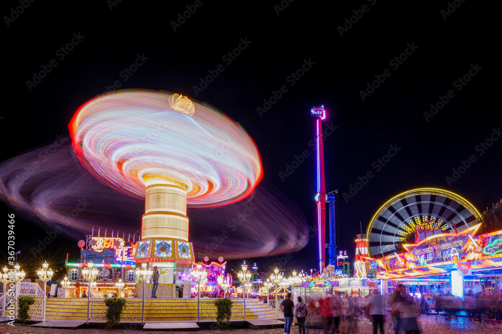 Φωτογραφία Night scenery atmosphere with colourful illumination motion of carousel in amusement park and background of Ferris wheel at Rheinkirmes funfair festival