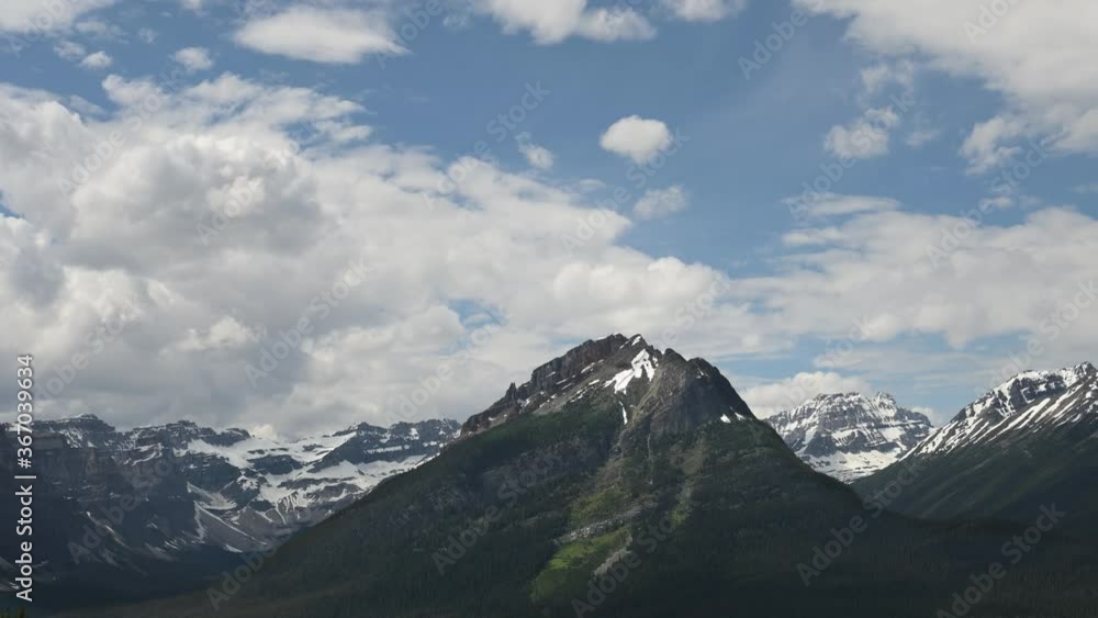 Time lapse of the clouds moving slowly over a triangle shaped mountain and a group of glacier covered mountains in the background.
Time lapse of the clouds moving slowly over a triangle shaped mountain and a group of glacier covered mountains in the background.