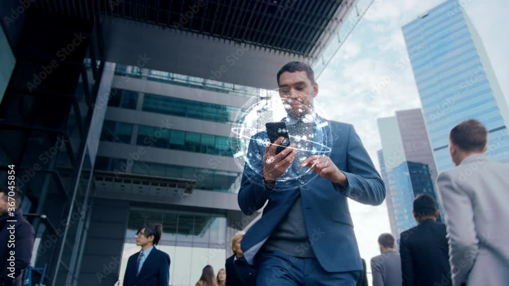 Handsome Businessman Uses Smartphone with Animated Infographics Showing Internet Icons, Walks through Crowded City Streets. Big Data, Information, e-Business Concept. Moving Low Angle Front View