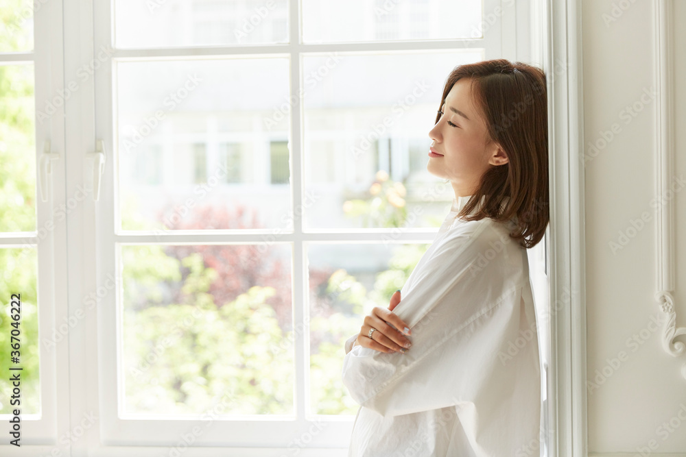 serene young asian woman staying at home leaning against window frame serene young asian woman staying at home leaning against window frame