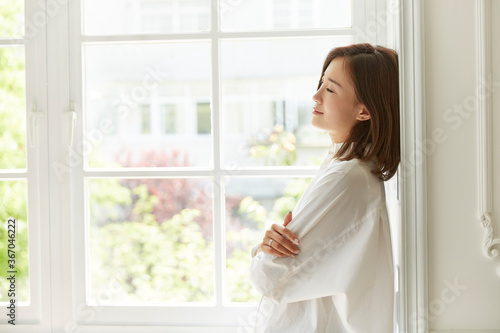 serene young asian woman staying at home leaning against window frame