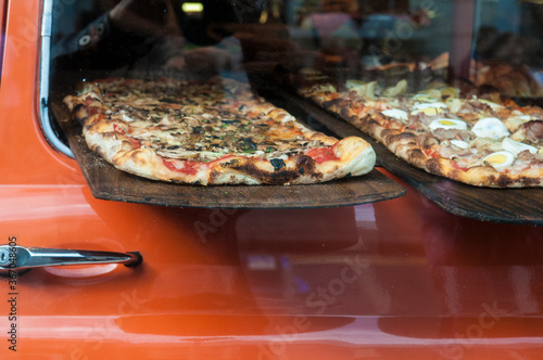 Delicious oven-fired pizza displayed on pizza peels supported by door of red car window. 