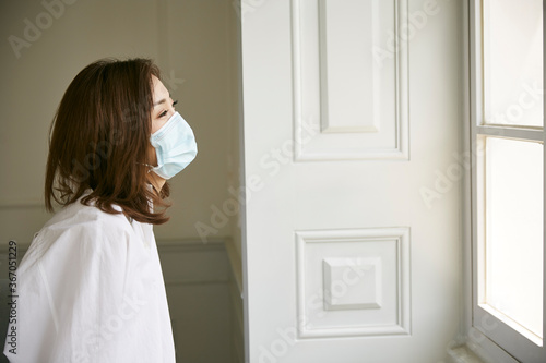 young asian woman wearing mask looking out of window