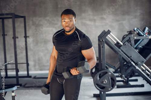 Sports man in the gym. A black man performs exercises. Guy in a black t-shirt