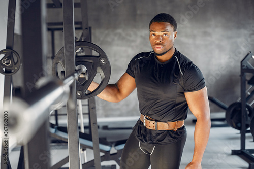 Sports man in the gym. A black man performs exercises. Guy in a black t-shirt