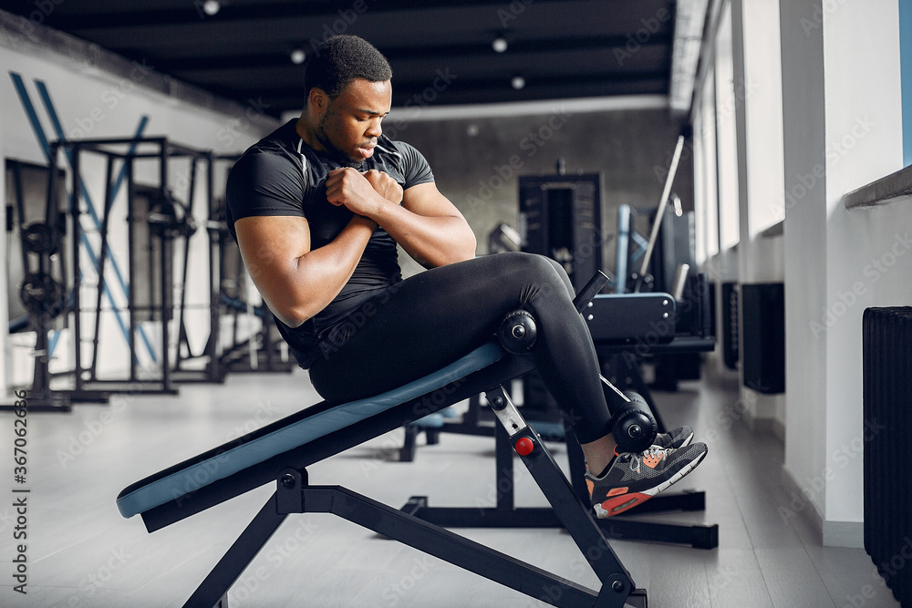 Sports man in the gym. A black man performs exercises. Guy in a black t-shirt