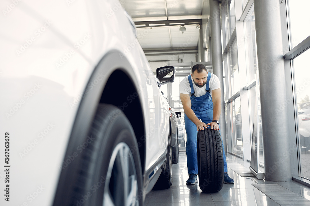 Wrker in a car salon. Expert checks the car. Man in a blue uniform. Wrker in a car salon. Expert checks the car. Man in a blue uniform.