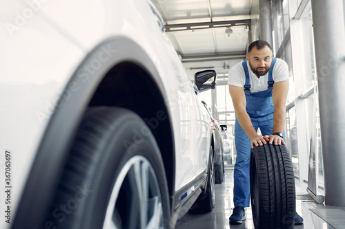 Wrker in a car salon. Expert checks the car. Man in a blue uniform.