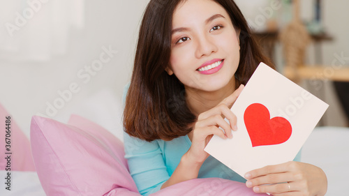 Young Asian woman holding love envelope when lying on bed.