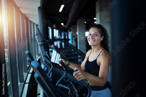 Sportswoman or athlete smiling on training while running on treadmill machine in the gym. Happy and positive people workout.