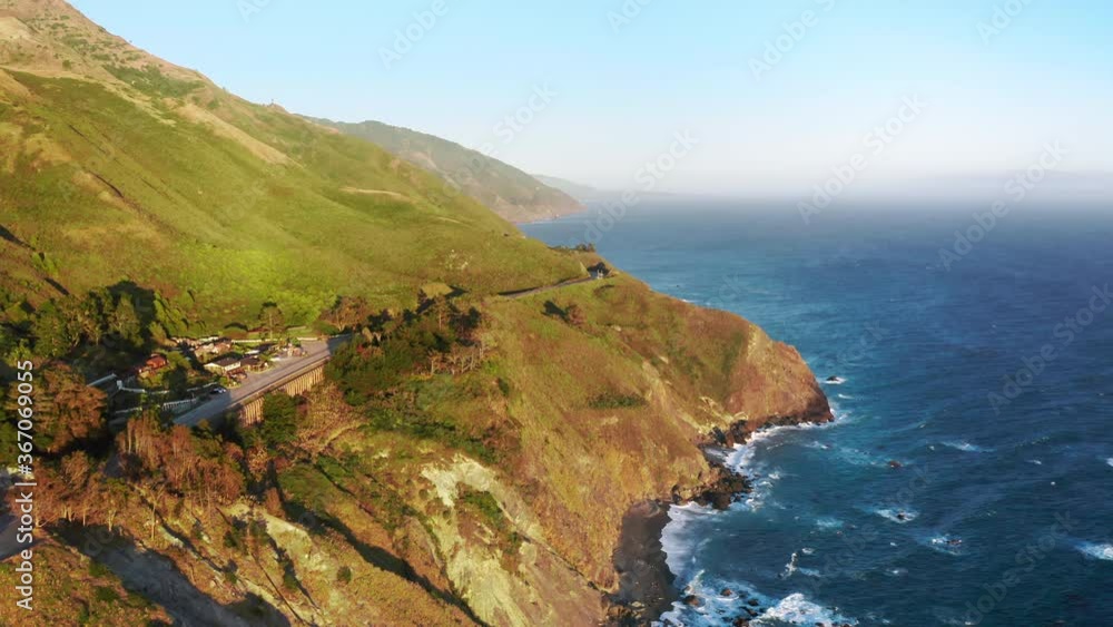 Famous west coastline, sunset view. 4K cinematic aerial of golden hour light covering the scenic blue ocean shore, with waves crashing on the picturesque sea rocks, USA. Summer road trip adventure Famous west coastline, sunset view. 4K cinematic aerial of golden hour light covering the scenic blue ocean shore, with waves crashing on the picturesque sea rocks, USA. Summer road trip adventure