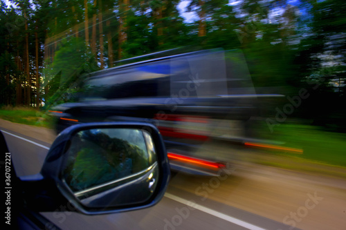 Overtaking a car at high speed in summer. Overtaking a car at high speed in summer. Signal red lights of a car on the background of the forest along the road. Motion blur