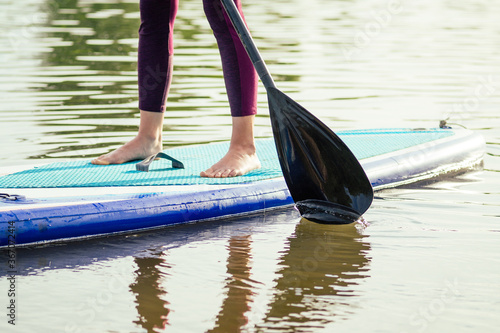 Stand up paddle boarding on a quiet sea lake , close-up of legs and water splash