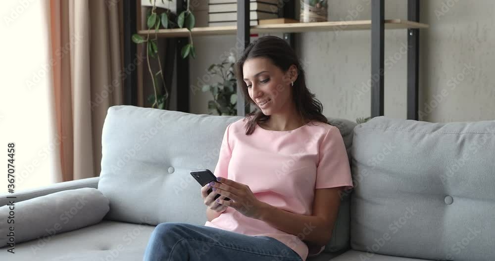 Indian woman sit on couch spend time using smart phone and internet connection smile looking at camera. Enjoy new cool app, every day easy convenient gadget usage for communication or business concept Indian woman sit on couch spend time using smart phone and internet connection smile looking at camera. Enjoy new cool app, every day easy convenient gadget usage for communication or business concept