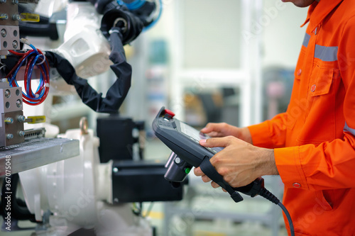 Smart factort concept: An engineer use handheld controller setting industrial robot in productionplant.