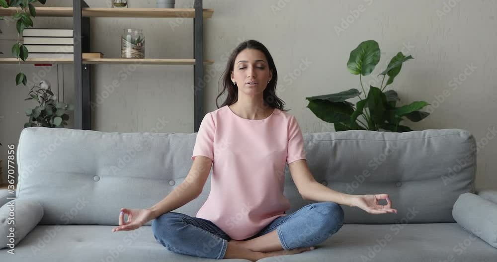 Mixed race Indian woman sit cross-legged on comfy sofa in living room closed eyes do meditation practice feels inner harmony and balance, improve self-conscious, mindfulness state, no stress concept Mixed race Indian woman sit cross-legged on comfy sofa in living room closed eyes do meditation practice feels inner harmony and balance, improve self-conscious, mindfulness state, no stress concept
