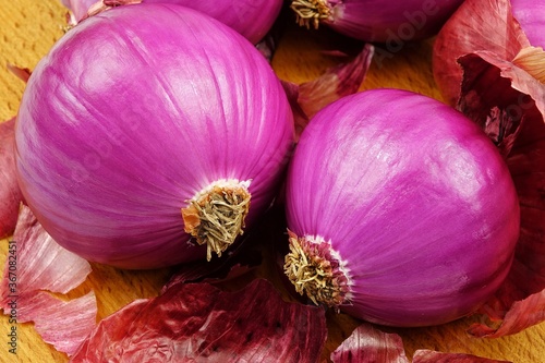 Red onions and dry onion skin are laid out on a wooden board, purple vegetable