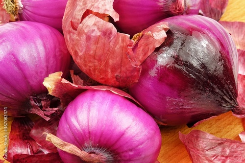 Red onions and dry onion skin are laid out on a wooden board, purple vegetable