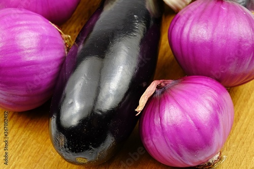 Red onions and eggplants are laid out on a wooden board  purple vegetable