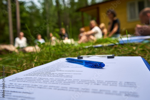 Pen on the paper in the garden. Seminar, people around. 