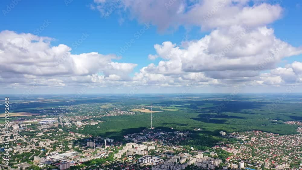 Panoramic view of a city among green nature. Cityscape under blue sky with white clouds. Beautiful scenery of a town near fields. Aerial view. Panoramic view of a city among green nature. Cityscape under blue sky with white clouds. Beautiful scenery of a town near fields. Aerial view.