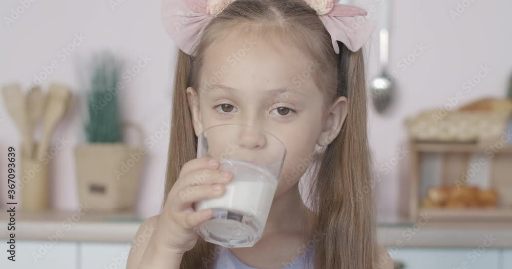 Close-up face of cute little girl drinking milk and smiling. Portrait of satisfied Caucasian brunette child with brown eyes enjoying healthful dairy product in the morning. Close-up face of cute little girl drinking milk and smiling. Portrait of satisfied Caucasian brunette child with brown eyes enjoying healthful dairy product in the morning.