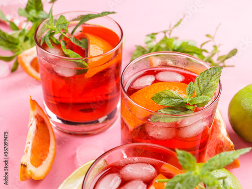 Fresh iced red cocktail in pink glasses with blood orange and lime on pink background garnished with mint leaves. Closeup