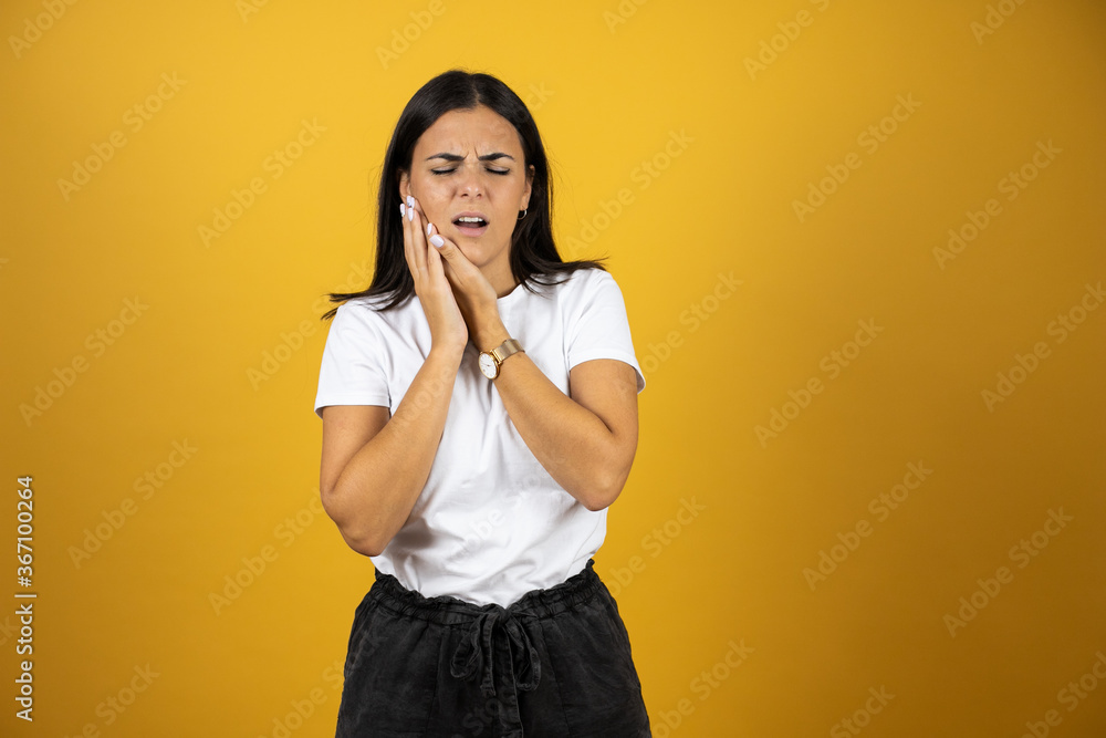 Beautiful woman wearing casual white t-shirt over isolated yellow background touching mouth with hand with painful expression because of toothache or dental illness on teeth Beautiful woman wearing casual white t-shirt over isolated yellow background touching mouth with hand with painful expression because of toothache or dental illness on teeth