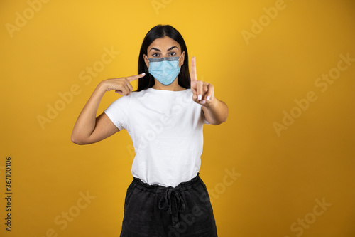 Young pretty woman wearing mask to protect herself from the coronavirus recommending using it to stop the pandemic. Covid-19