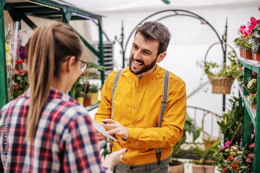 Young smiling male employee talking with her boss and showing him offers that customers want. Hothouse interior. Young smiling male employee talking with her boss and showing him offers that customers want. Hothouse interior.