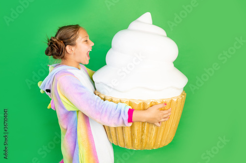 Valokuva a little girl on a green isolated background in a bright suit holds a huge cake