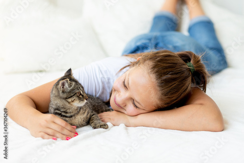 A child is torturing an animal, a little girl with a cat is lying on the bed, the concept of a child's friendship with animals