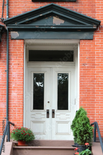 White double wooden vintage entry door decorated with triangular fronton and flower pots with flowers. New York. USA.