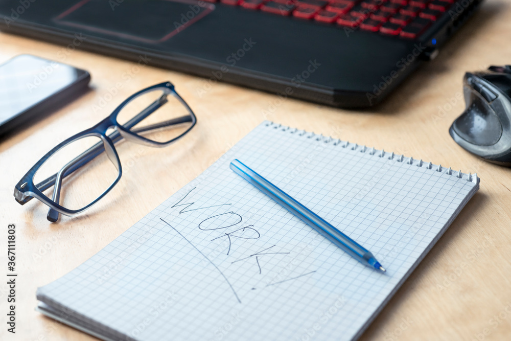 On the table near the laptop is a notebook in which the word work is written. Top view layout of a daily work plan On the table near the laptop is a notebook in which the word work is written. Top view layout of a daily work plan